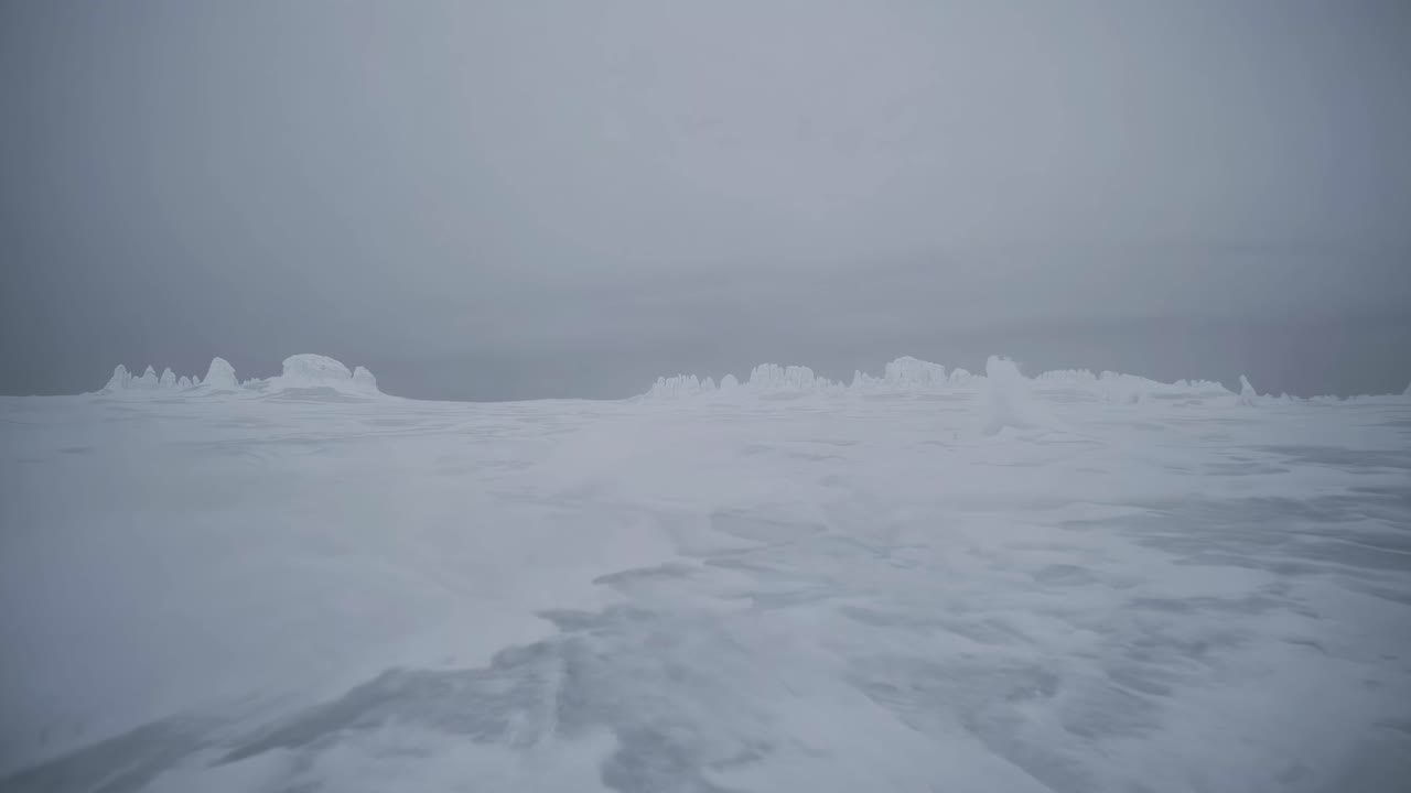 A serene, low-angle video shot of a vast, snow-covered landscape under a gray sky