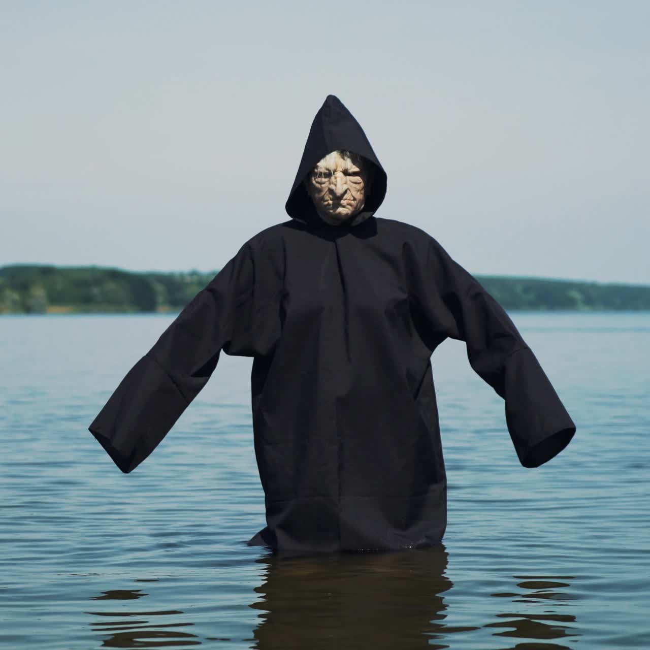 Scary figure in black mantle in the river. Halloween costume