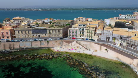 Revealing-drone-shot-of-Syracuse-coastline,-historic-city-on-the-Italian-island-of-Sicily-with-the-Ionian-Sea-in-the-distance