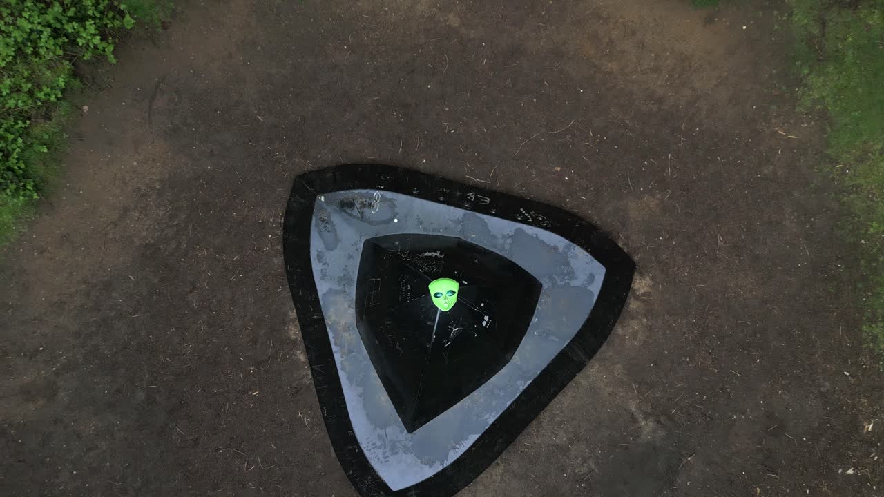 vista aérea ascendente mirando hacia abajo sobre la máscara alienígena divertida colocada en el bosque de rendlesham platillo volador aterrizaje sire