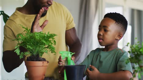 African-american-father-and-son-watering-plant-pot-and-high-fiving-each-other-at-home