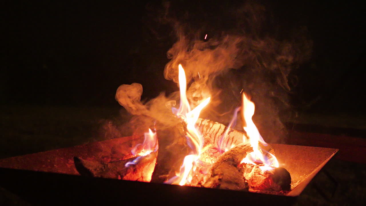 Wood logs burning in fireplace at night, creating smoke and embers