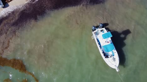 Mientras-La-Cámara-Se-Eleva-Por-Encima-Del-Océano-Reluciente,-Se-Puede-Ver-Un-Bote-Solitario-Flotando-Tranquilamente-En-Las-Aguas-Cristalinas-De-Cancún,-México