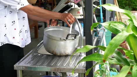 person washing stainless steel pot in garden kitchen, handheld view