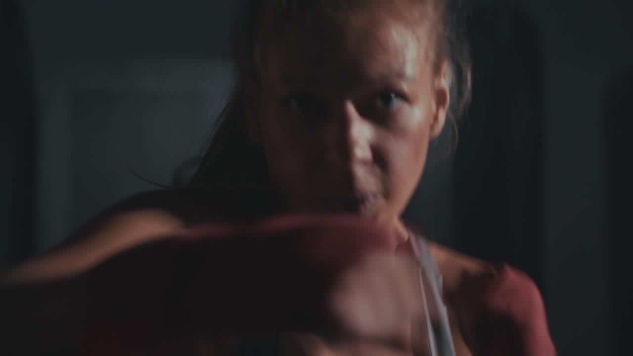 Close-up of a Woman Boxer Training with Intense Focus in a Dark Gym
