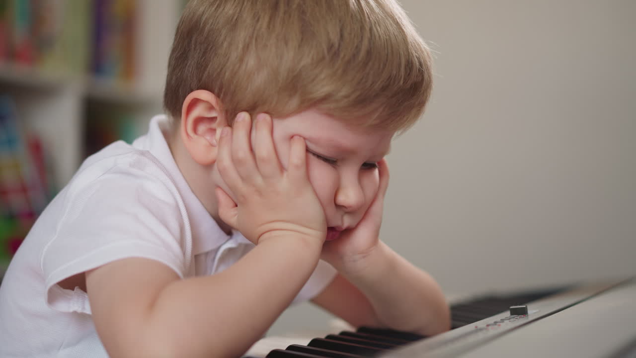 Little boy leans on hands and breathes out sadly at piano