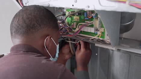 Man-with-mask-sticks-cables-from-damaged-washing-machine,-view-to-electrical-board,-close-up-socket