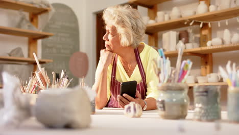 pensive biracial female potter with gray hair looking ahead in pottery studio, slow motion