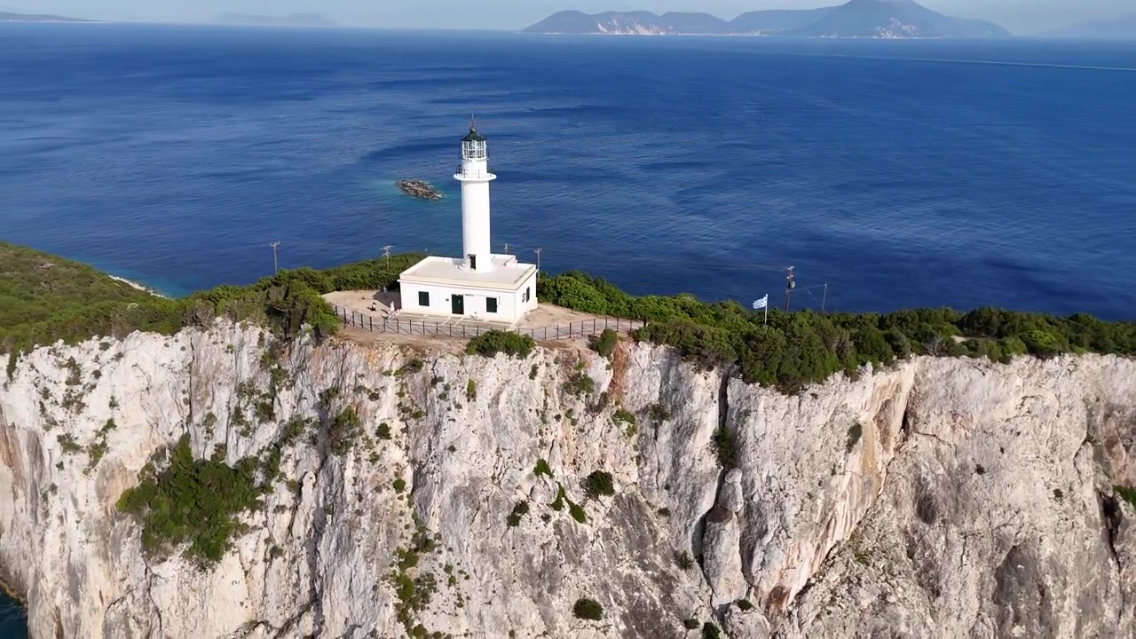 Sorvolo aereo con drone di un faro bianco su una scogliera rocciosa a picco sull'acqua blu. Paesaggio costiero suggestivo con vista sull'oceano.