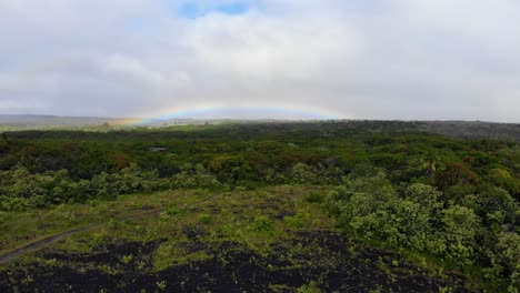 Langsamer-Aufstieg-über-Straße,-Wald-Und-Lavafelder-Mit-Regenbogen-Im-Hintergrund