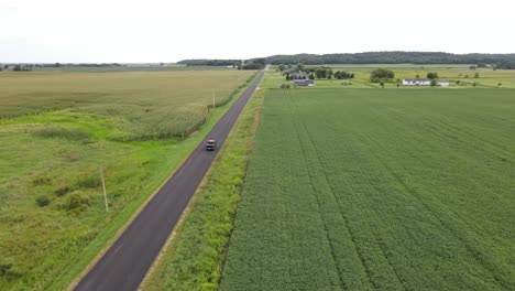 drone following a car driving along a rural road in the middle of farmer's fields with various crops, aerial view