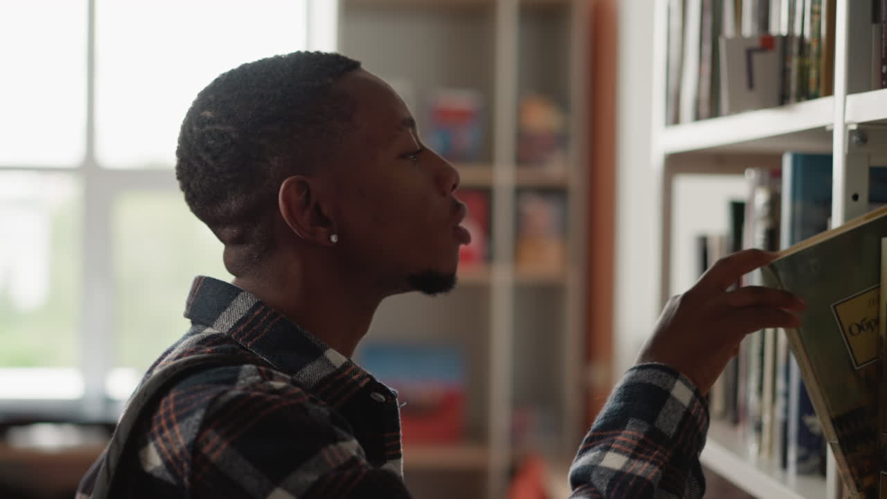 el estudiante toma un libro del estante de la biblioteca. el hombre afroamericano encuentra un libro de texto para escribir la tesis en el centro de información de la universidad. el chico elige una novela