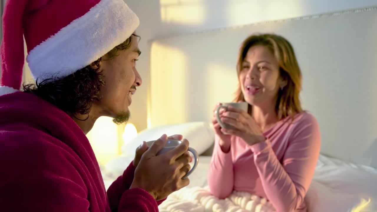 Couple entering bedroom, sharing coffee and croissants, wearing red bathrobe and Santa hat
