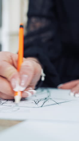 hands of a fashion designer with a beautiful manicure draw a sketch with a pencil. professional dressmaker creates a stylish design of a new dress on a sheet of paper. close-up vertical video