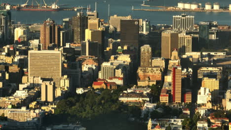 Elevated-footage-of-high-rise-buildings-in-city-centre-lit-by-sun-and-harbour-in-background.-Cape-Town,-South-Africa