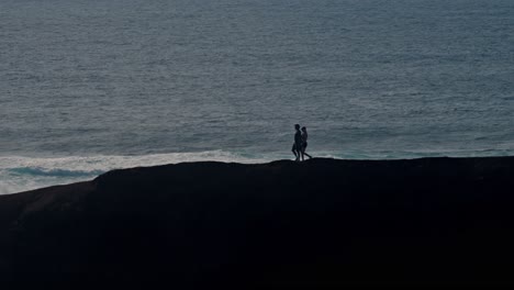 A young couple walks hand in hand along a rugged volcanic cliff overlooking the Atlantic Ocean in Lanzarote, Canary Islands, Spain.