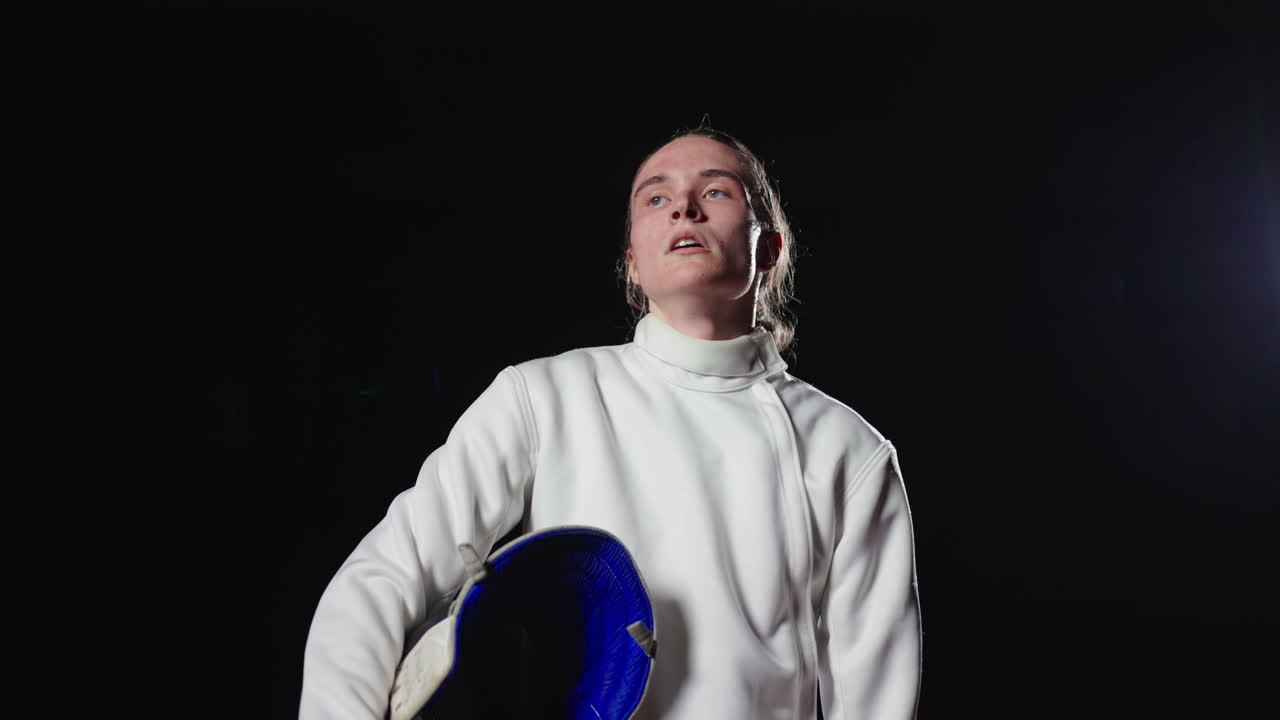 молодая фехтовальщица в белой форме и черной маске, готовящаяся к соревнованию