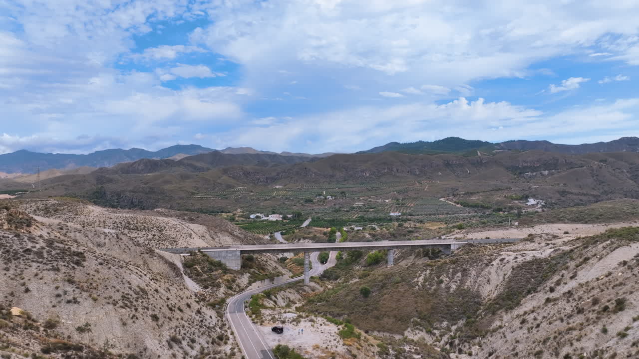 Flight reverses from a pristine newly constructed rail bridge revealing a road below and a vast rugged background landscape under a searing hot sky Sorbas Almeria Espana Spain