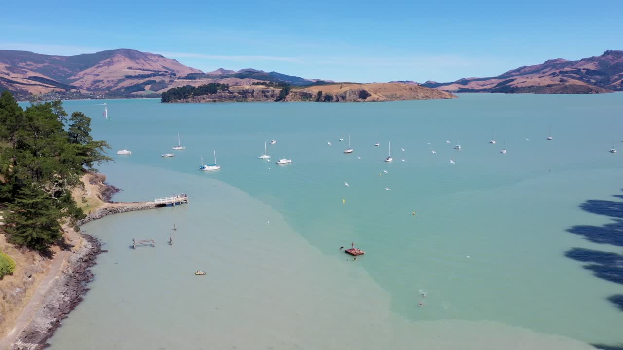 Drone video with tilt up flying over car park, beach and out to sea with island and mountains in background
