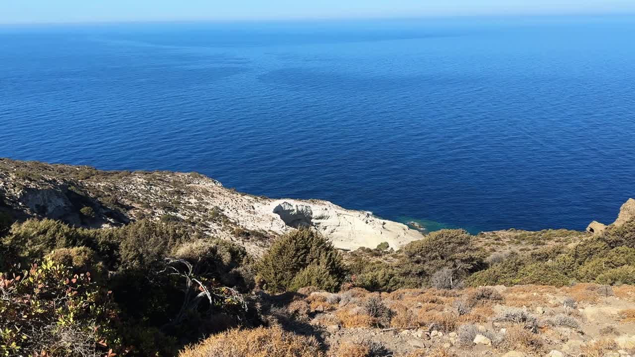 A distant view of a cave entrance framed by the shimmering blue ocean beyond.