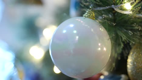 close-up of a white bulb hanging on a christmas tree as the tree lights flicker casting a golden glow