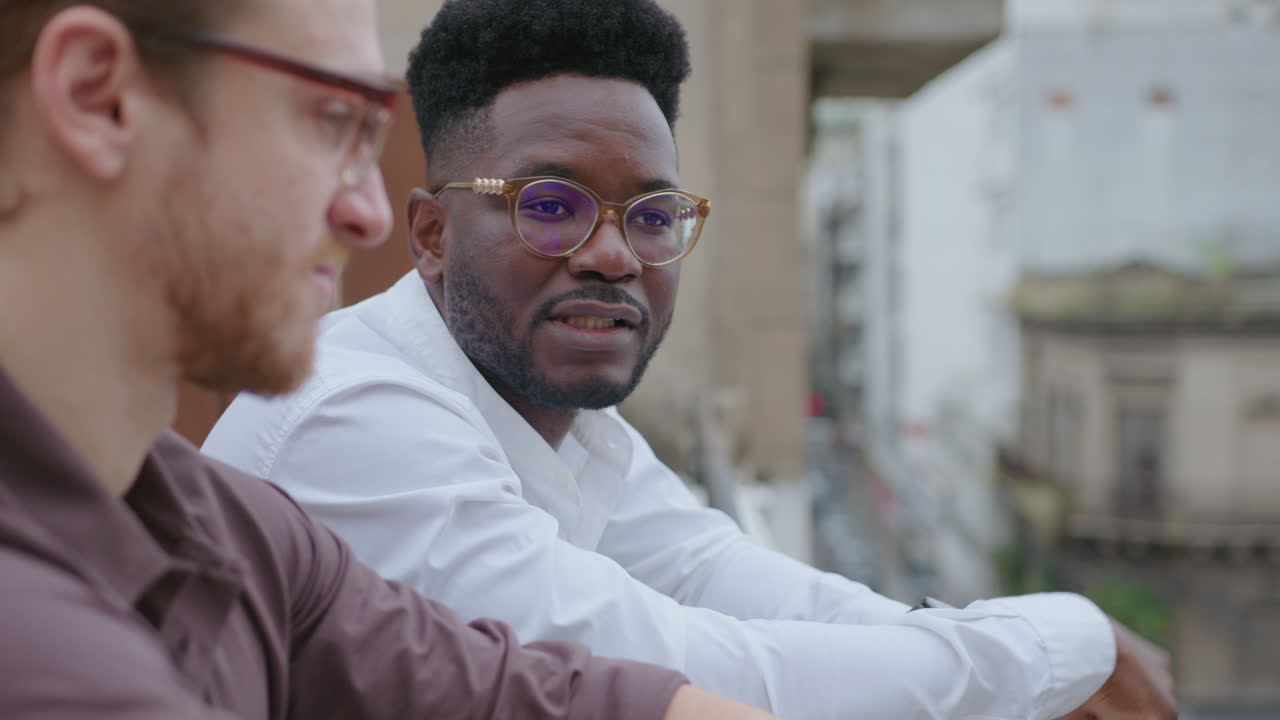 un hombre de negocios afroamericano hablando con un colega en un tejado urbano.