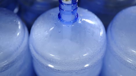 una vista de cerca de una máquina automatizada que llena grandes contenedores de agua azul en una instalación de embotellado de agua