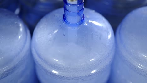 a close-up view of an automated machine filling large blue water containers in a water bottling facility