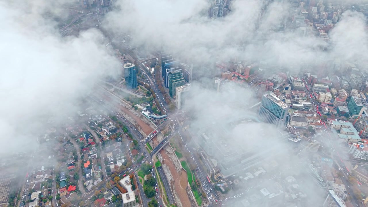 Vuelo aéreo lento de un paisaje urbano sobre las nubes con tráfico y el río Mapocho, Santiago de Chile.