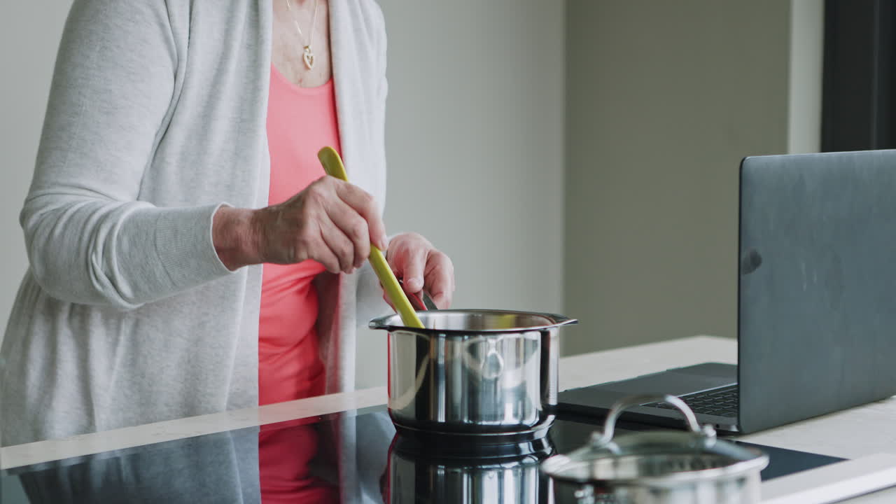 Senior woman cooking while using a laptop