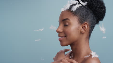 slow motion portrait beautiful african american woman feathers falling on smooth skin touching bare shoulders enjoying natural skincare beauty gently caressing body in blue background
