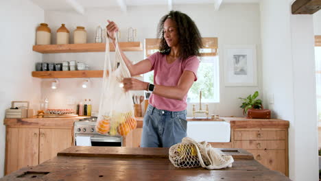 unpacking groceries from reusable bags, woman smiling in kitchen, at home