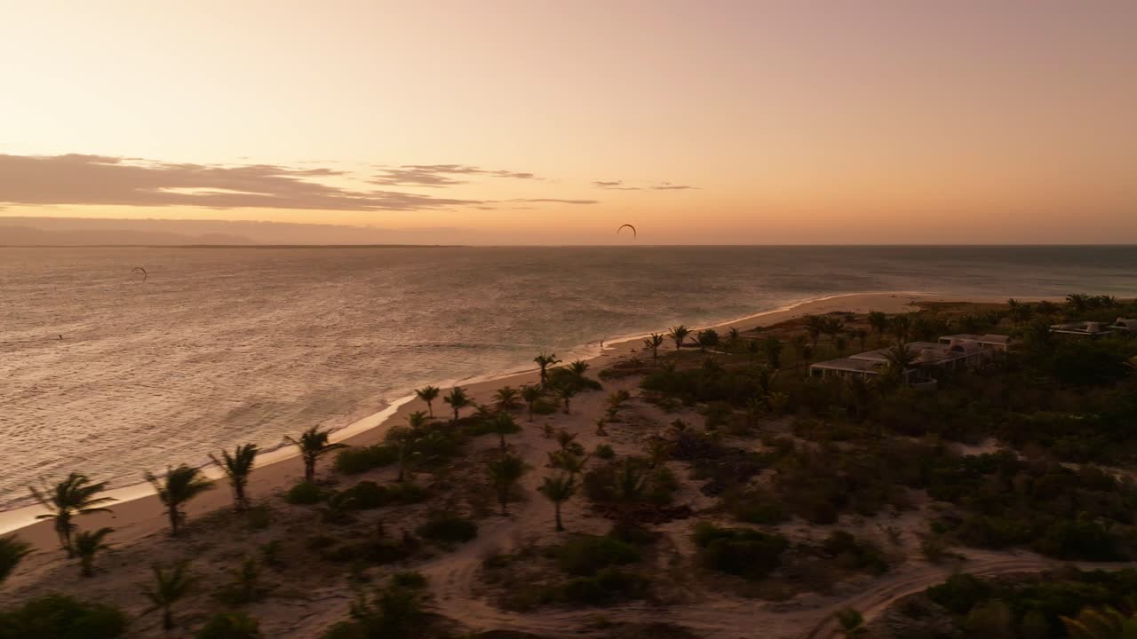 Golden sunset lights a private island with palm trees during a drone flight from sea to shore