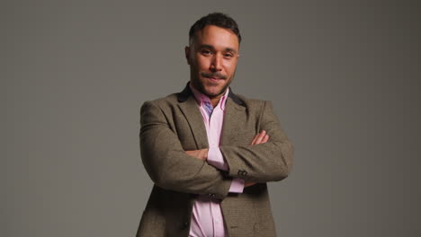 studio portrait of smiling mature male teacher wearing jacket folding arms standing against grey background