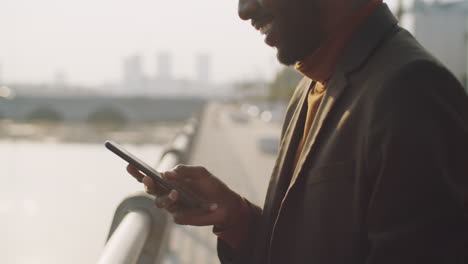 Hombre-De-Negocios-Afroamericano-Escribiendo-En-Un-Teléfono-Inteligente-Al-Aire-Libre