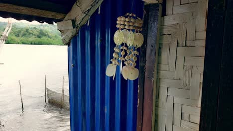 cerca de una campana de viento hecha de capiz balanceándose salvajemente en la brisa y colgada en una cabaña nativa con vistas al mar, isla sincera momento de vida