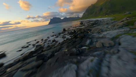 speed flight over coastline of lofoten with rocks in water and green mountain slope at golden sunset - forward drone movement