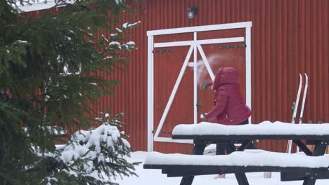 woman throwing a snowball in slow motion in front of a red wooden house in norway