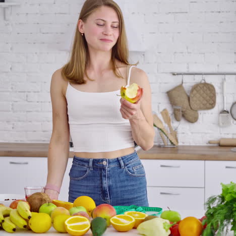 losing weight concept. young woman eating fruit in the kitchen. beautiful model in jeans standing at the table full of organic vitamins.