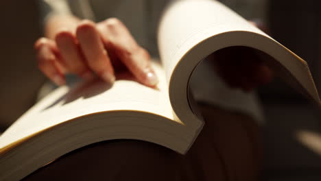 un primer plano de una mano girando suavemente una página en un ambiente de lectura sereno.