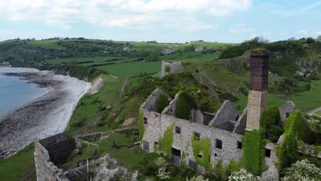 Abandoned-overgrown-ivy-covered-desolate-countryside-historical-Welsh-coastal-brick-factory-mill-aerial-view-slow-fly-over-roof