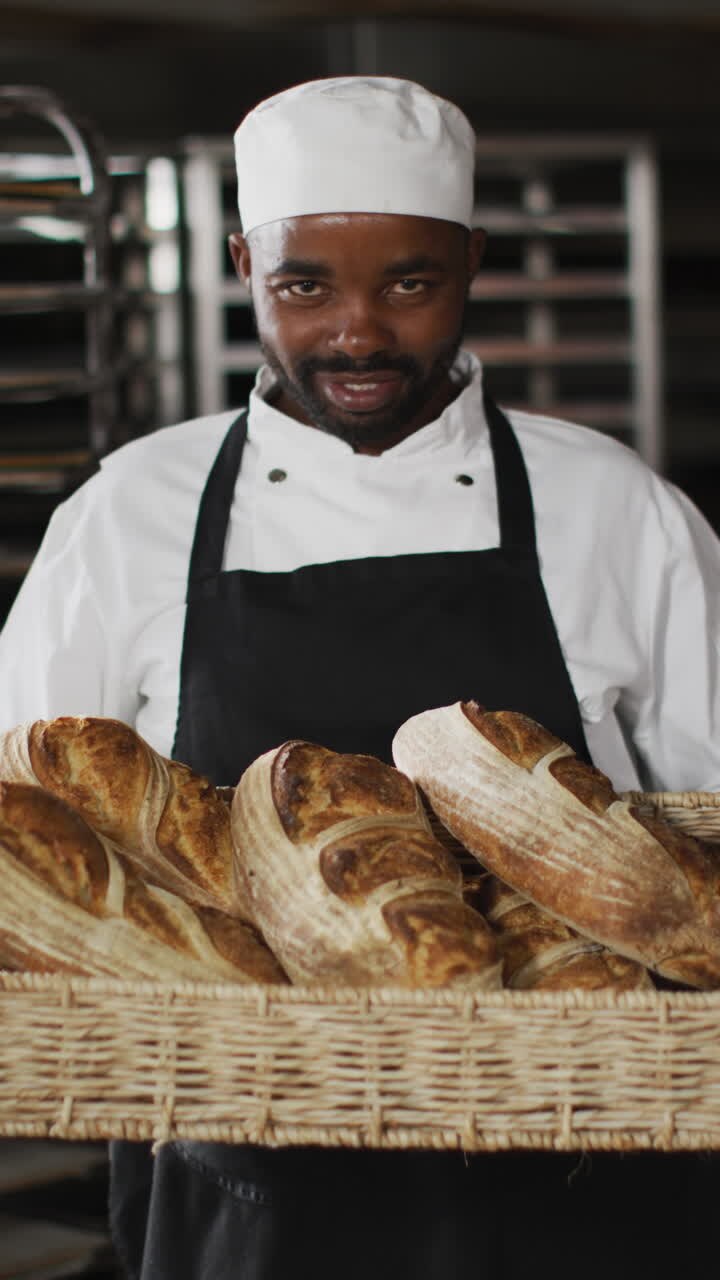 Vertical video of portrait of happy african american male baker with bread in bakery