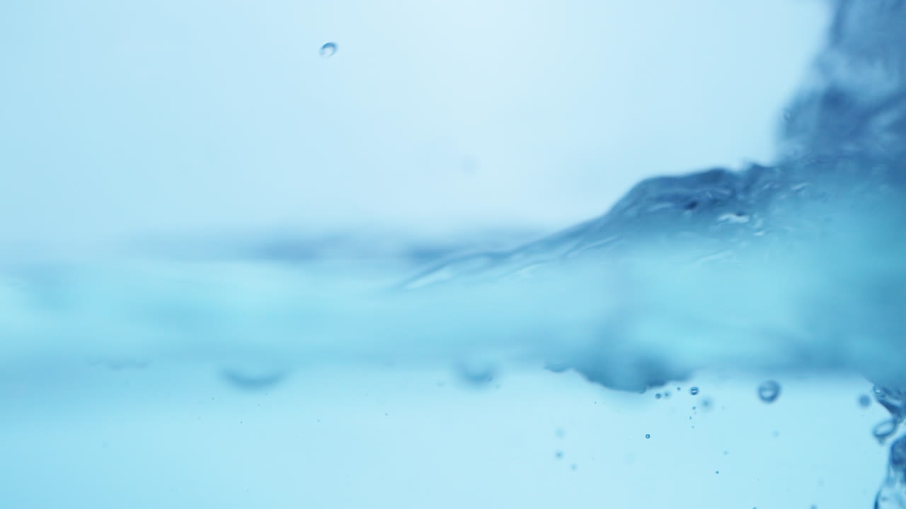 Smooth waves roll across the surface of clear blue water, capturing the serene and flowing essence of natural, fresh liquid.