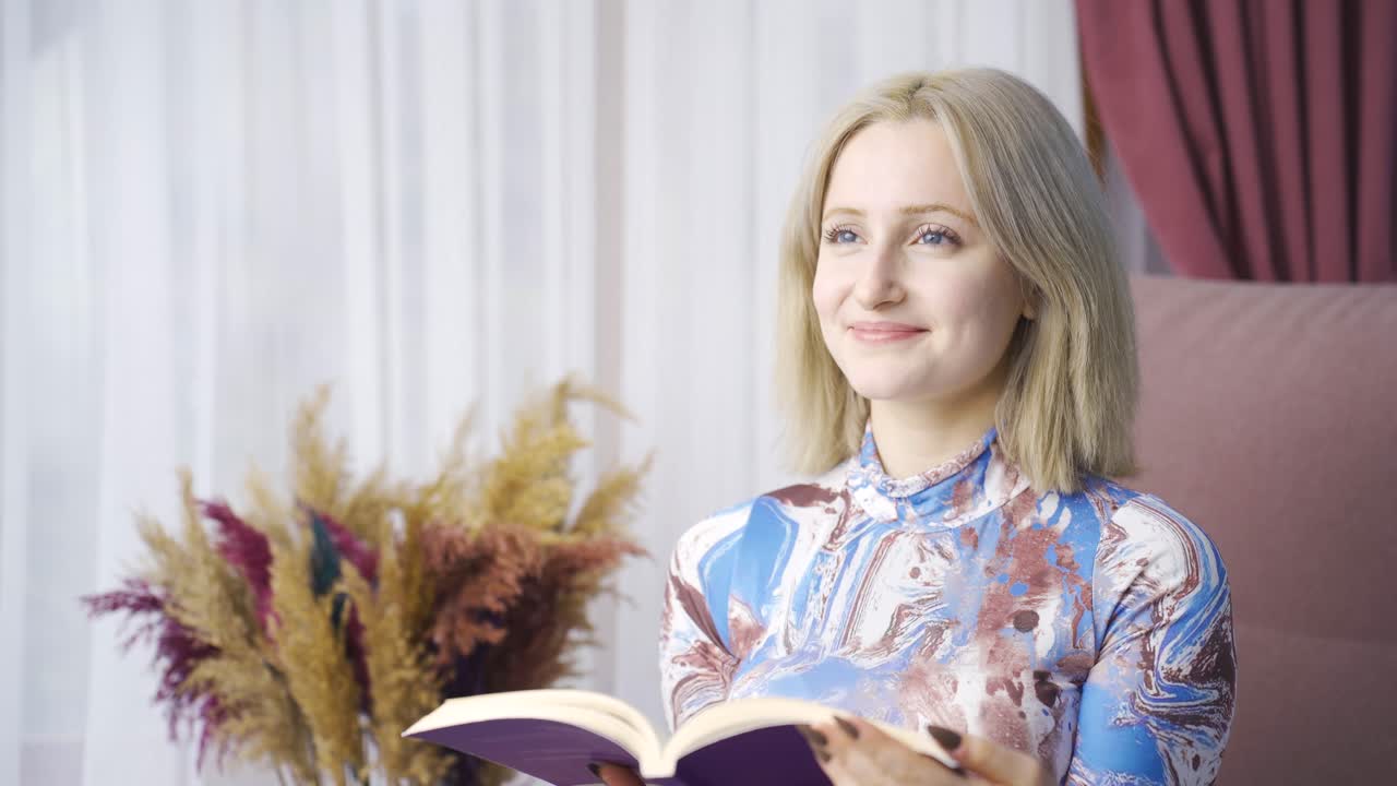 아름다운 젊은 여성이 집에서 편안하고 평화롭게 책을 읽고 있습니다.