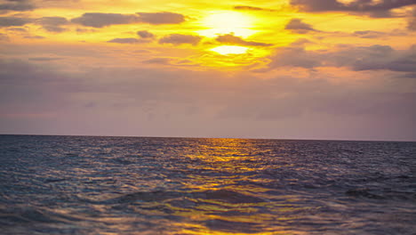 a golden cloudscape sunset over choppy ocean water with the colors reflecting off the water - time lapse