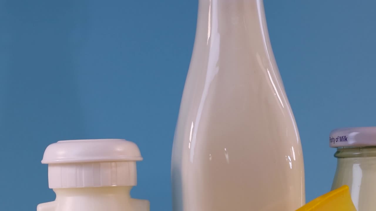Close-up of various dairy bottles and cheese against a blue backdrop.