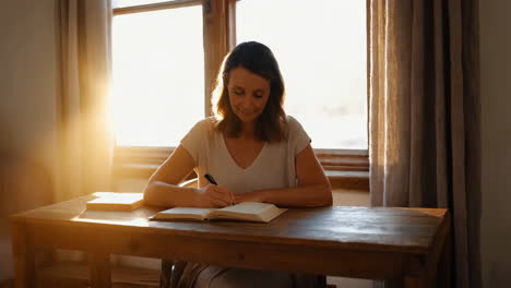 woman writing in a journal by a sunny window