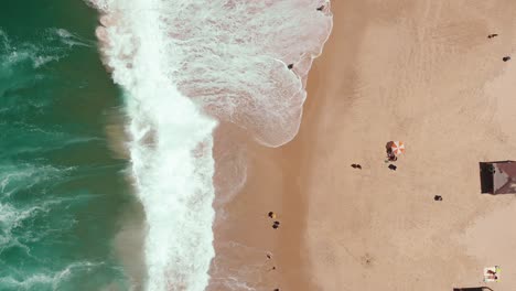 static aerial drone showing endless wild sea waves breaking on the sandy coast line while people hang out on the beach