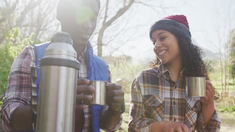 una pareja diversa sonriente bebiendo té y caminando por el campo