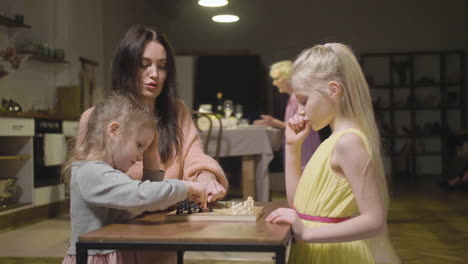 mother and her two little daughters playing chess at home